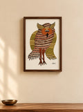 Framed wall art featuring a stylized owl with intricate geometric patterns in brown, gold, and cream, displayed on a beige wall above a wooden surface.