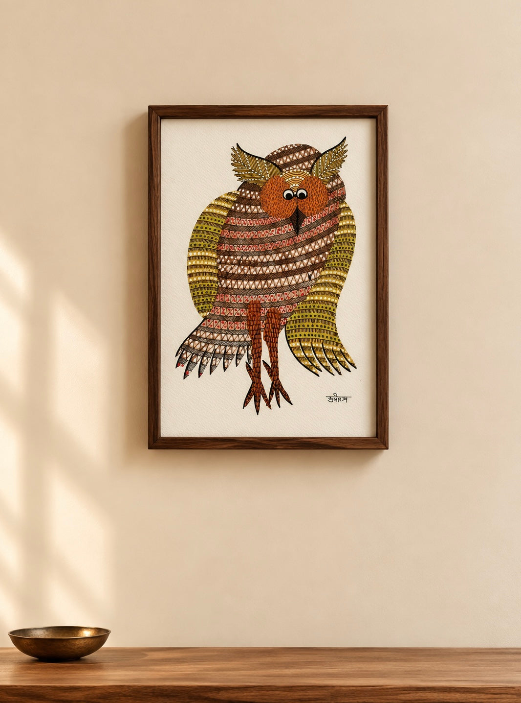 Framed wall art featuring a stylized owl with intricate geometric patterns in brown, gold, and cream, displayed on a beige wall above a wooden surface.