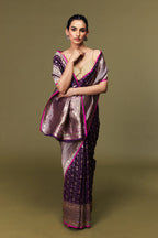 Model draped in handwoven Banarasi Katan silk saree in purple with pink border and golden zari motifs.